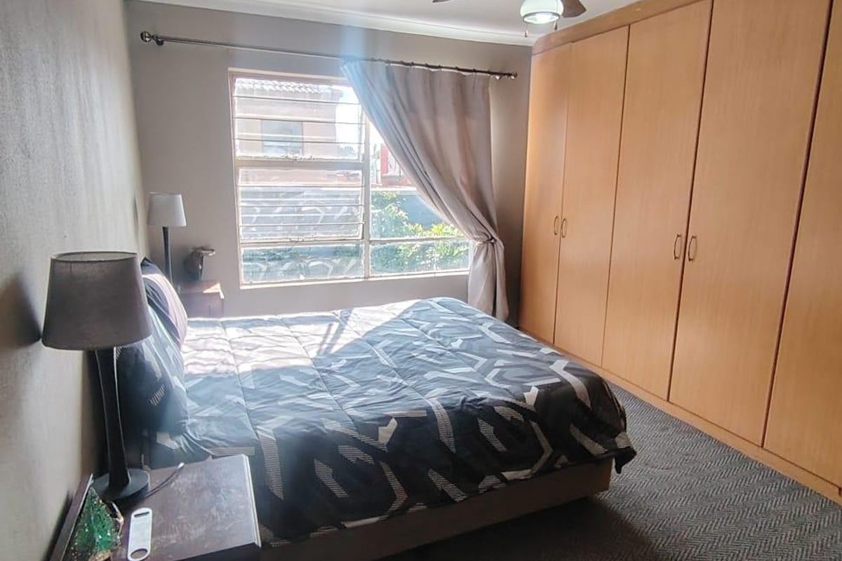 A functional bedroom featuring built-in wooden cupboards, a ceiling fan, and carpeted flooring, providing ample storage and comfortable living space.