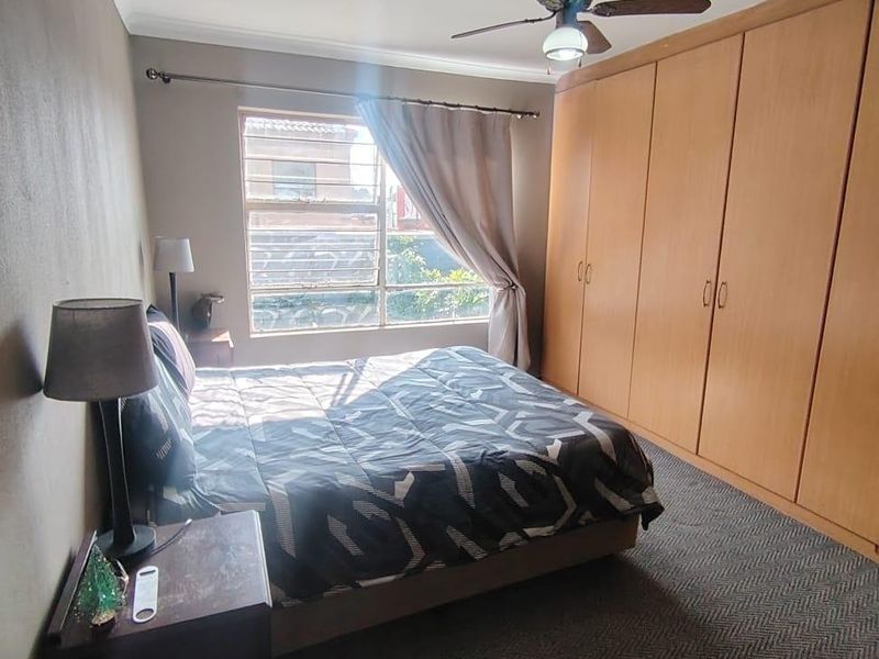 A functional bedroom featuring built-in wooden cupboards, a ceiling fan, and carpeted flooring, providing ample storage and comfortable living space.