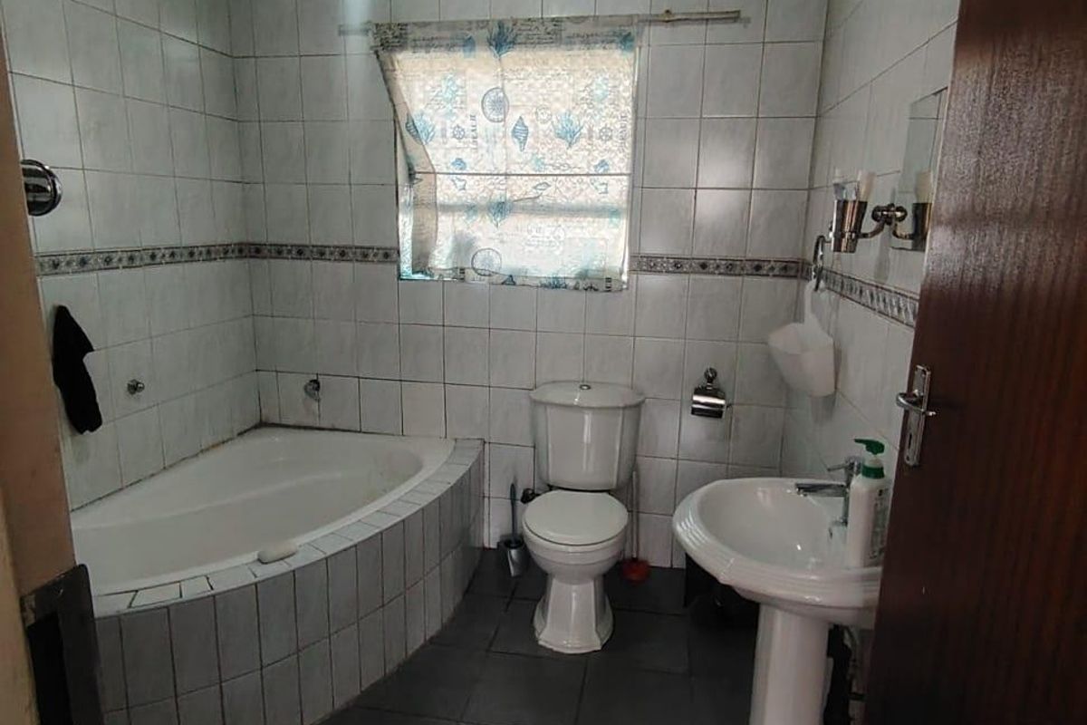 A functional bathroom featuring a built-in bathtub, pedestal sink, and toilet, finished with tiled walls and flooring.