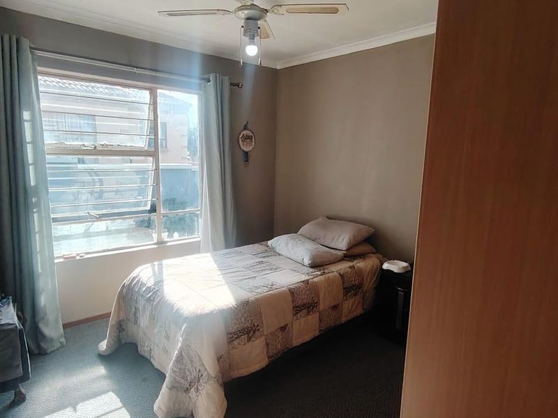 A functional bedroom featuring a ceiling fan, louvered windows for ventilation, and built-in cupboard storage.