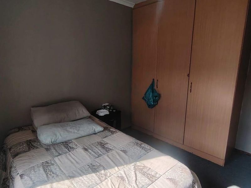 A functional bedroom featuring a large built-in wooden wardrobe and a ceiling fan, providing essential storage and climate control.
