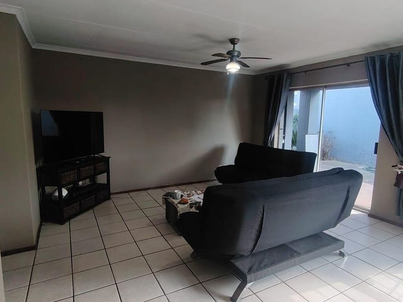 A living room featuring ceramic floor tiles, a ceiling fan, and a sliding glass door providing access to the outdoor area.