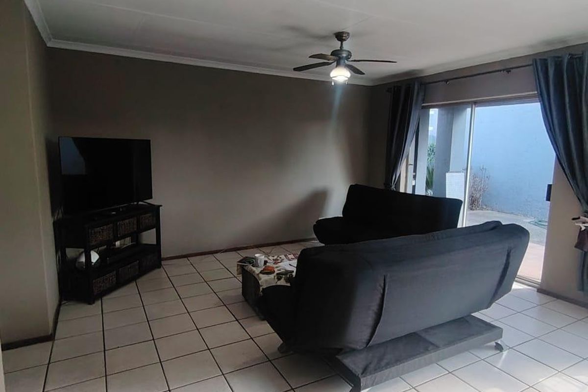 A living room featuring ceramic floor tiles, a ceiling fan, and a sliding glass door providing access to the outdoor area.