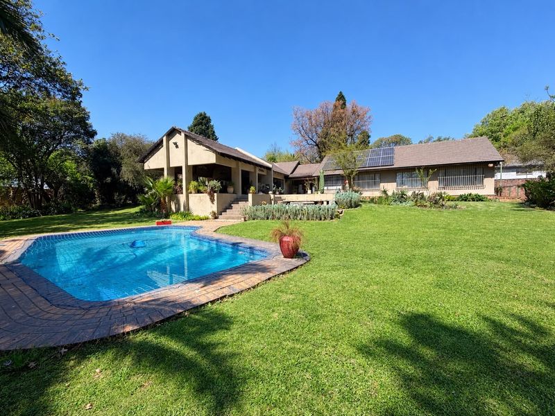 Spacious rear garden featuring a swimming pool, covered patio area, and a main residence equipped with roof-mounted solar panels.