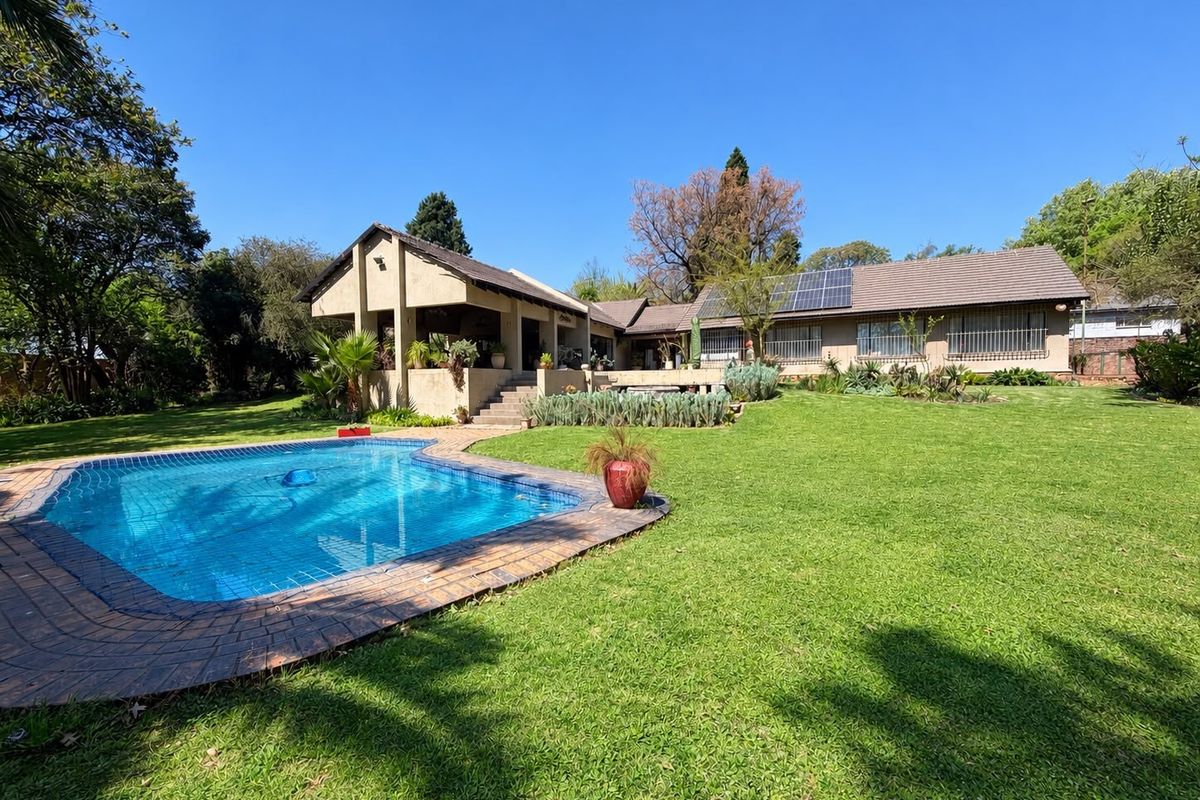 Spacious rear garden featuring a swimming pool, covered patio area, and a main residence equipped with roof-mounted solar panels.