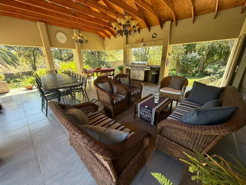 Spacious covered patio featuring exposed timber beam ceilings, tiled flooring, and a built-in braai area, perfect for outdoor entertaining.