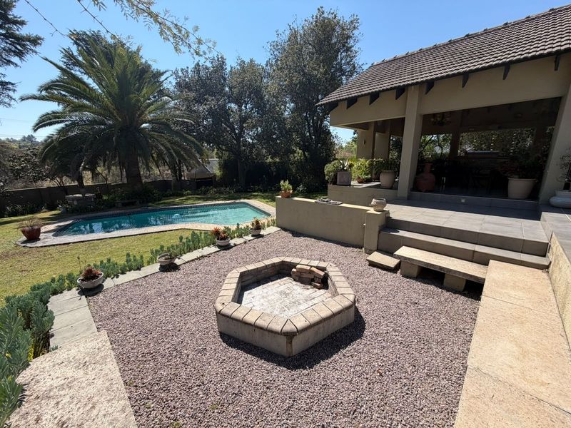 Rear garden area featuring a swimming pool, covered patio, and a central built-in stone fire pit with gravel landscaping.