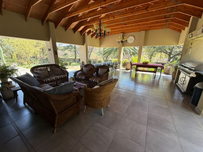 Spacious covered patio featuring an exposed timber beam ceiling, tiled flooring, and a built-in gas grill, perfect for outdoor entertaining.