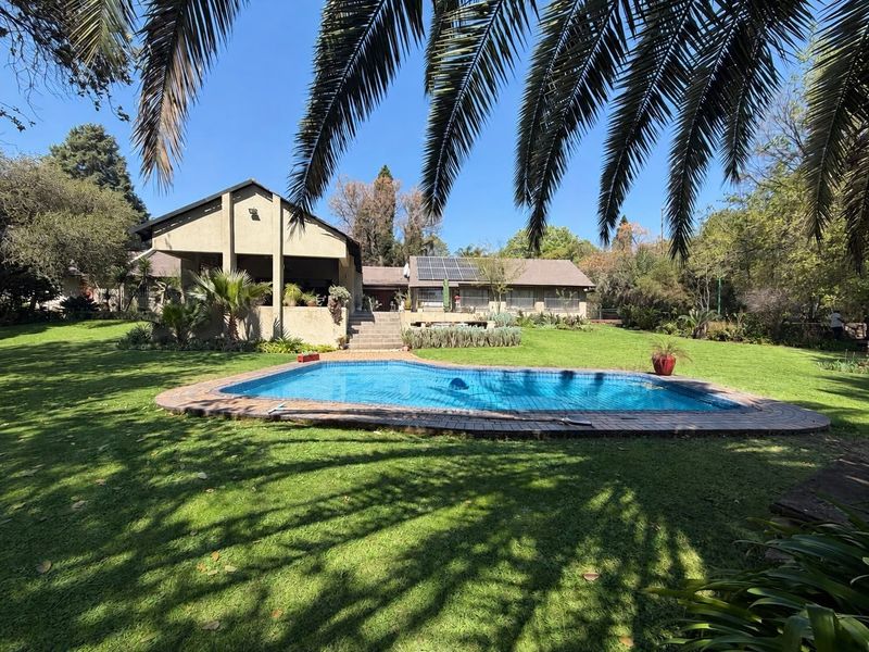 Spacious rear garden featuring a swimming pool, covered patio area, and solar panels installed on the main house roof.