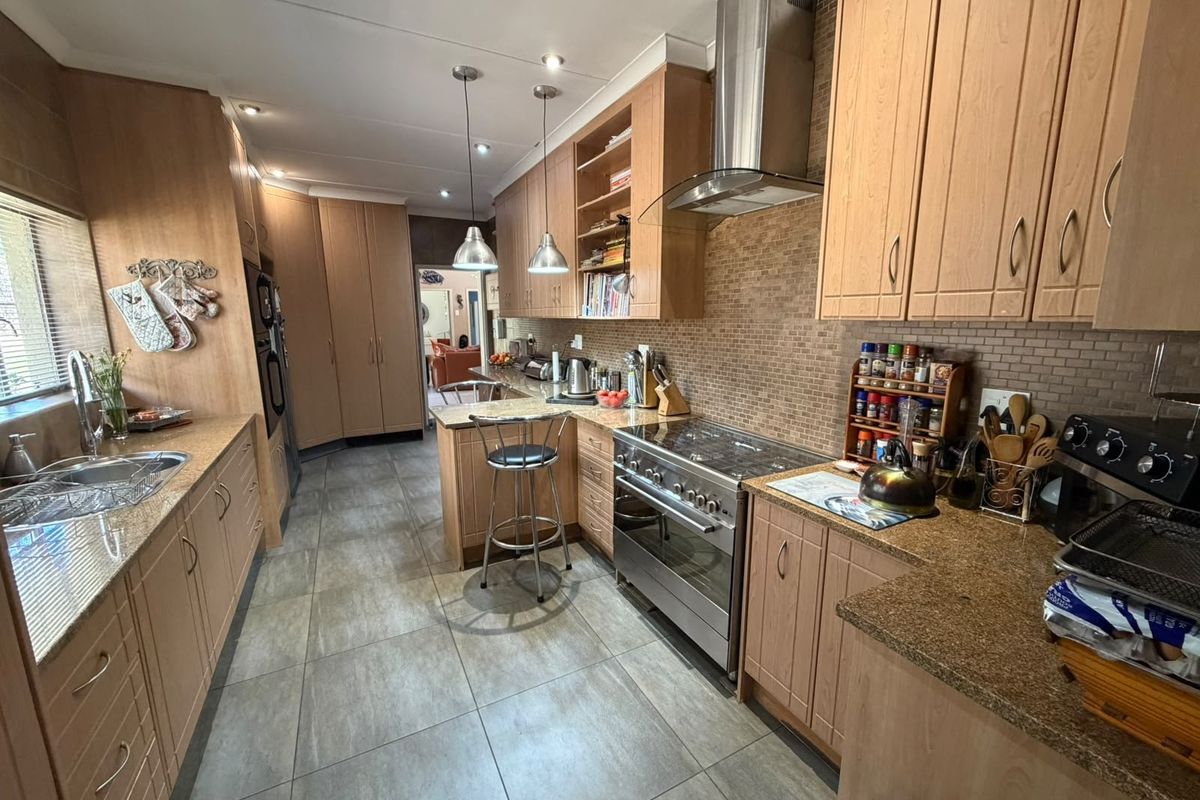 A well-appointed kitchen featuring granite countertops, stainless steel appliances, tiled backsplash, and ample built-in cabinetry with modern lighting.