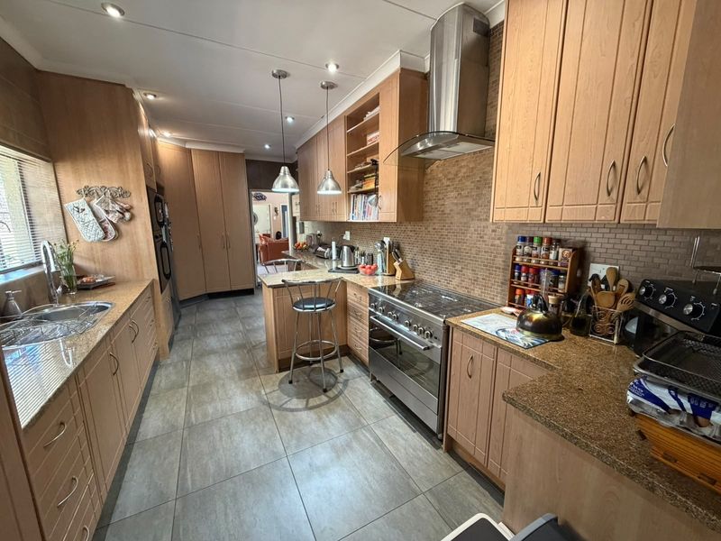 A well-appointed kitchen featuring granite countertops, stainless steel appliances, tiled backsplash, and ample built-in cabinetry with modern lighting.