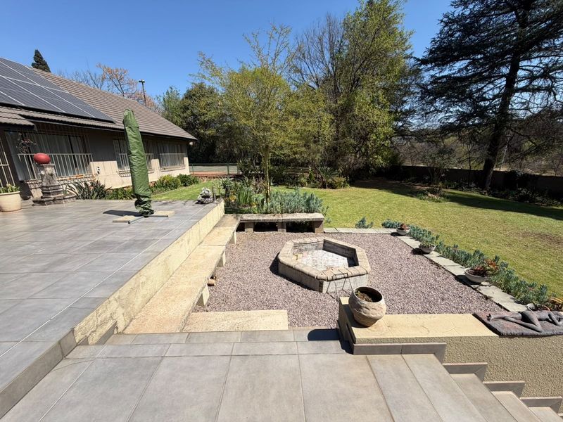 Spacious rear garden featuring a large tiled patio, built-in fire pit area, and landscaped lawn with mature trees.