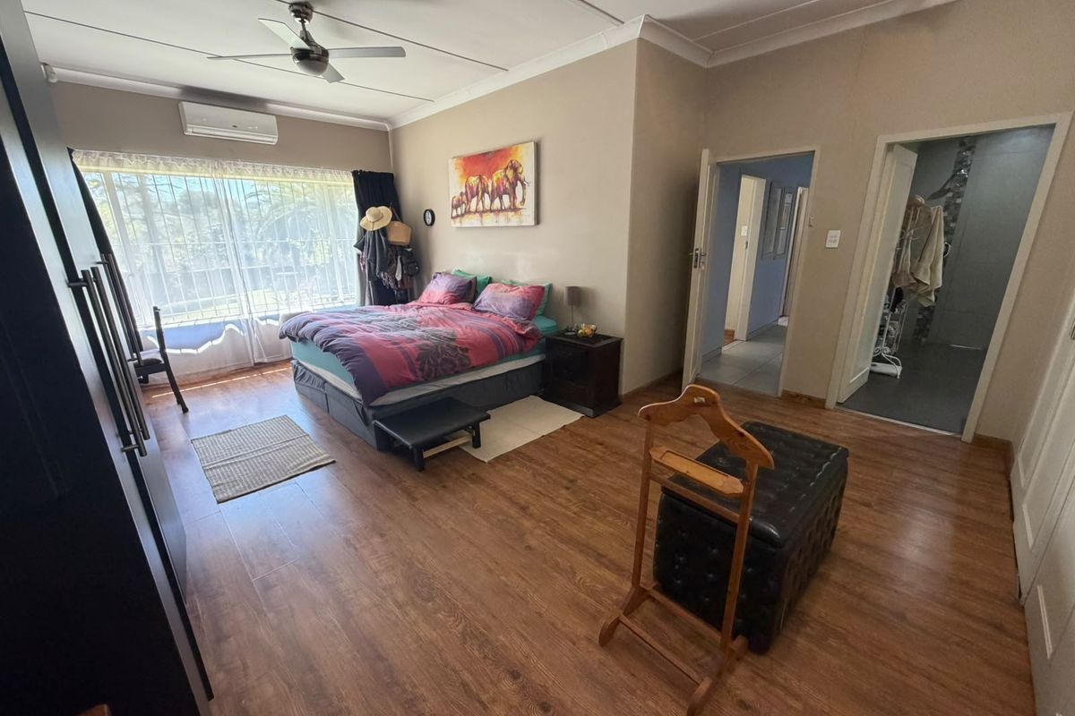 Spacious bedroom featuring laminate flooring, built-in cupboards, a ceiling fan, and a split-system air conditioner, with direct access to an en-suite bathroom.