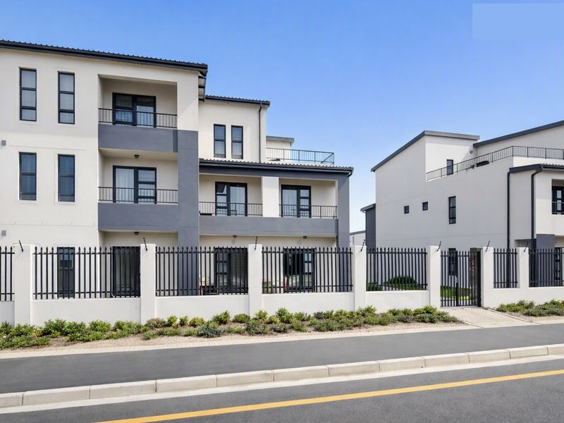 A modern multi-story apartment complex featuring clean architectural lines, private balconies, and secure perimeter fencing along the street front.