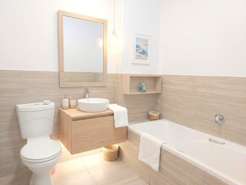 Modern bathroom featuring a wall-mounted vanity with a vessel sink, a built-in bathtub, and neutral-toned wall and floor tiling.
