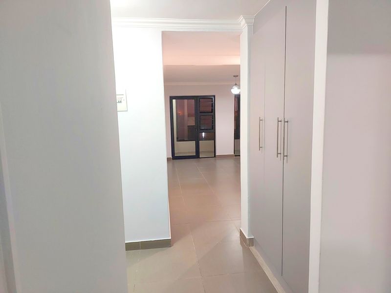 A clean, empty hallway featuring neutral tiled flooring, built-in storage cupboards, and a glass panel door leading to an adjacent living space.