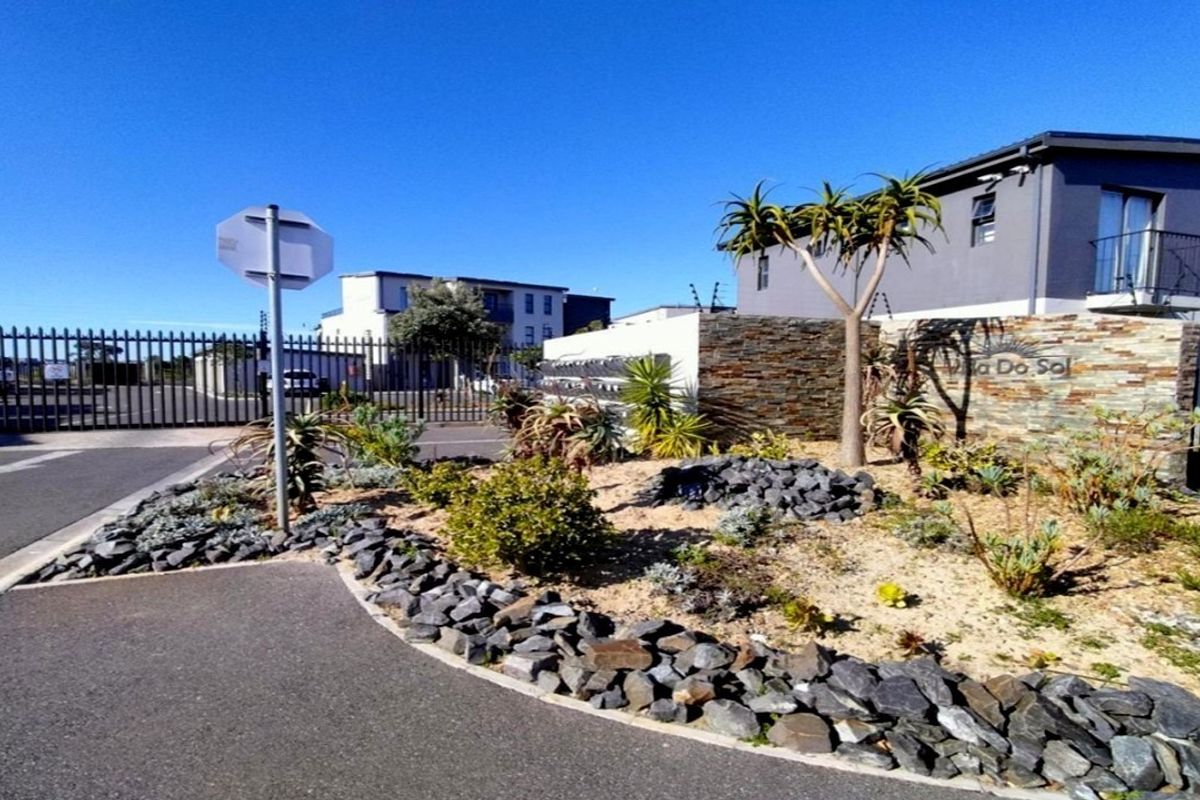Front entrance view of the apartment complex featuring stone-clad signage, secure perimeter fencing, and a well-maintained landscaped garden area.