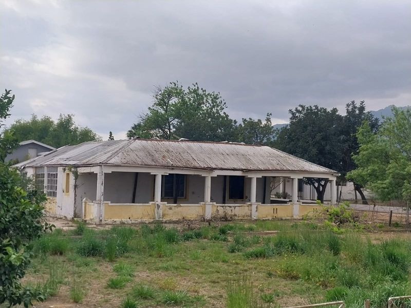 A single-story detached house featuring a covered veranda and corrugated metal roof, currently showing significant signs of exterior wear and structural weathering.