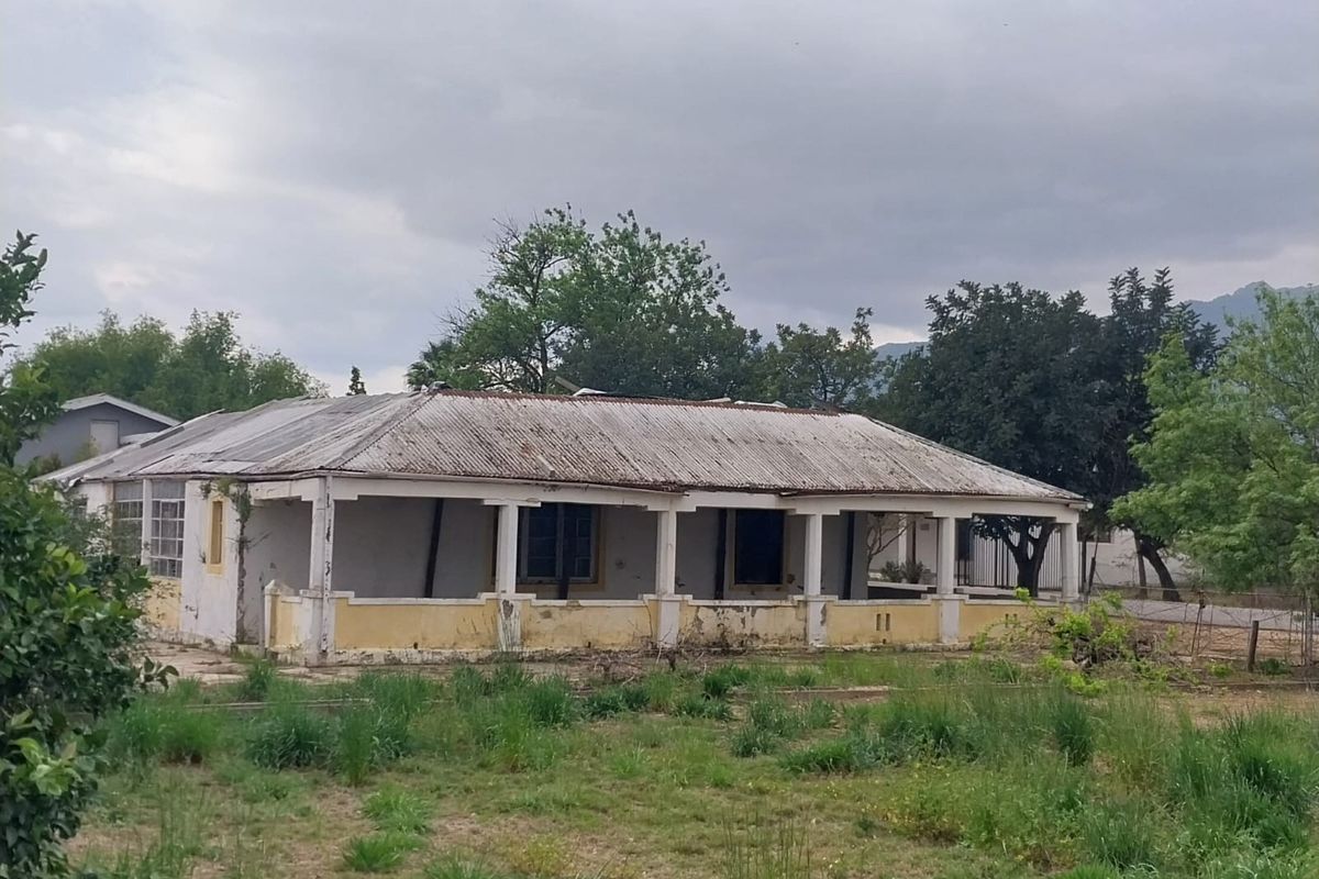 A single-story detached house featuring a covered veranda and corrugated metal roof, currently showing significant signs of exterior wear and structural weathering.
