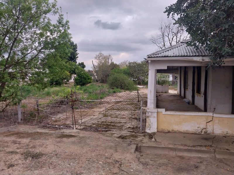 Rear view of a property featuring a covered veranda, chain-link fencing, and significant signs of exterior wear and structural weathering.