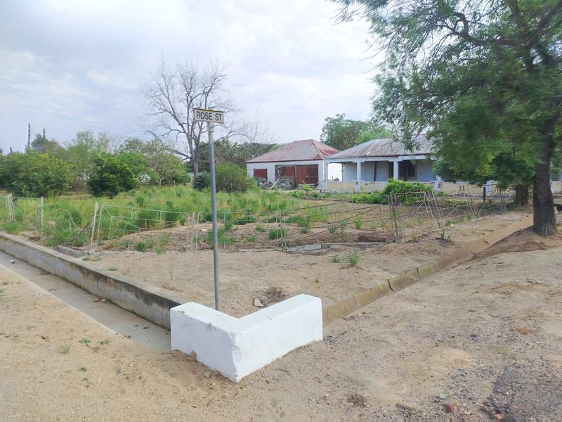 A street-level view of a property corner featuring a street sign, wire fencing, and a view of the main dwelling and detached outbuilding.