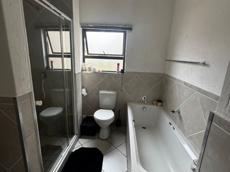 A functional bathroom featuring a separate shower enclosure, a standard bathtub, and a toilet with neutral wall and floor tiling.