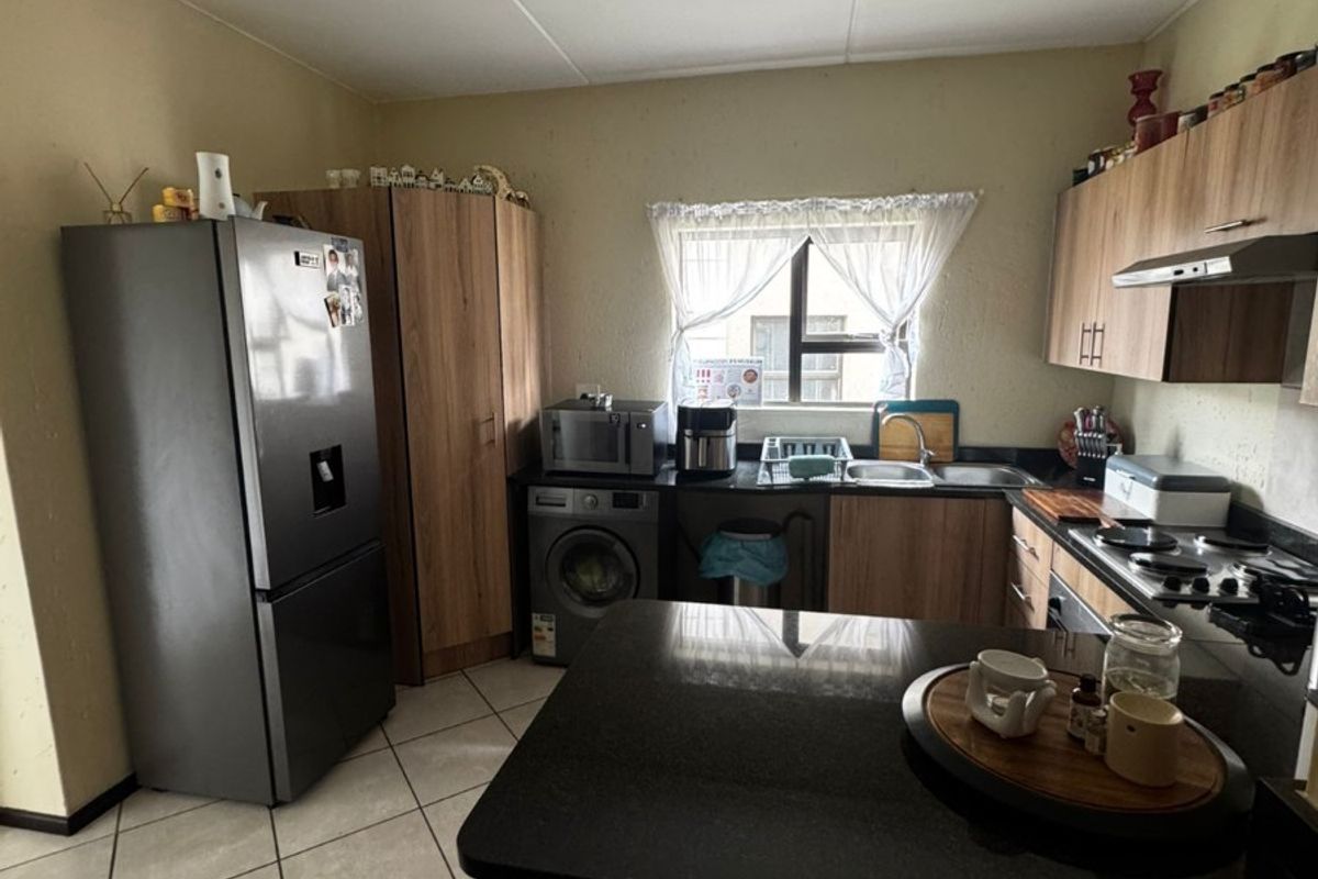 Functional kitchen featuring wood-finish cabinetry, granite countertops, a gas hob, extractor fan, and tiled flooring with space for integrated appliances.