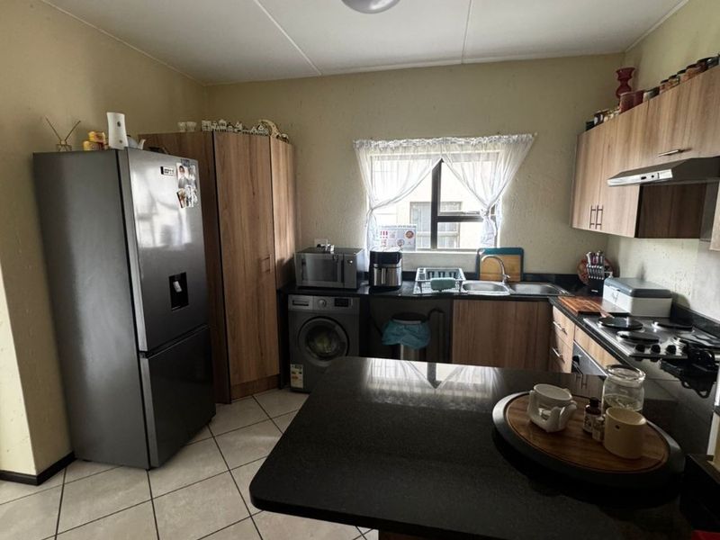 Functional kitchen featuring wood-finish cabinetry, granite countertops, a gas hob, extractor fan, and tiled flooring with space for integrated appliances.
