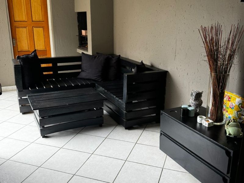A covered patio area featuring tiled flooring, a built-in fireplace, and a wooden door leading to the interior.
