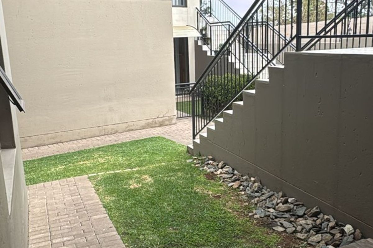 Rear exterior view of an apartment complex featuring a paved walkway, small lawn area, and an external metal staircase with railings.