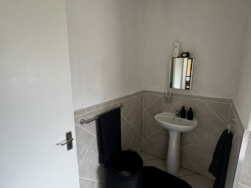 A compact guest bathroom featuring a pedestal sink, neutral wall and floor tiling, and a functional layout.