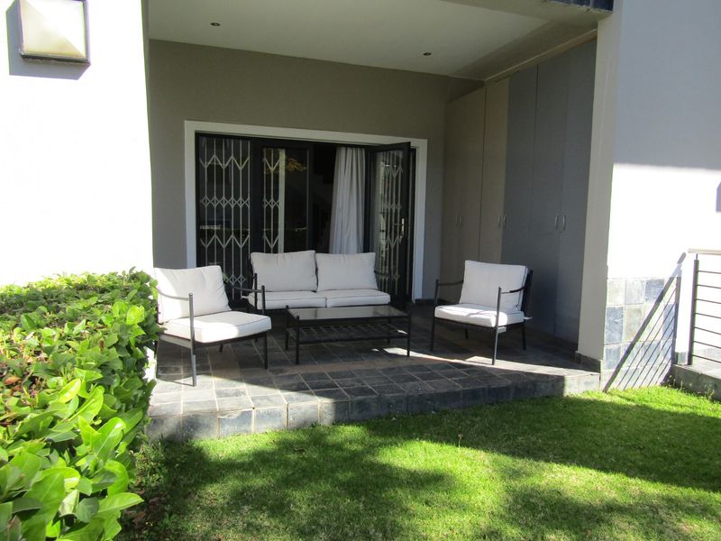 A covered patio area featuring tiled flooring, recessed lighting, and built-in storage cupboards, providing direct access to the garden through sliding glass doors.