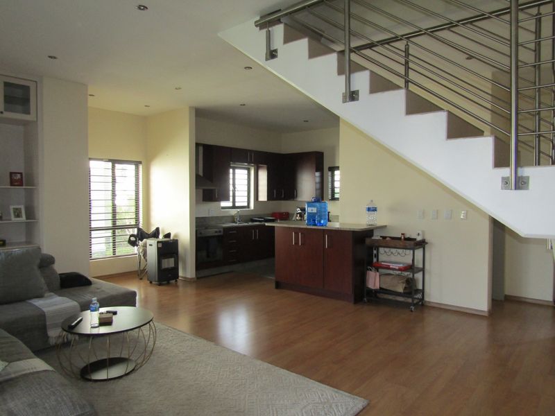 Open-plan living area featuring laminate flooring, a modern kitchen with built-in cabinetry, and a staircase with a stainless steel railing.
