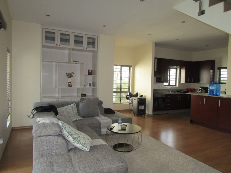 Open-plan living area featuring laminate flooring, recessed lighting, a built-in shelving unit, and a functional kitchen with dark cabinetry and stone countertops.