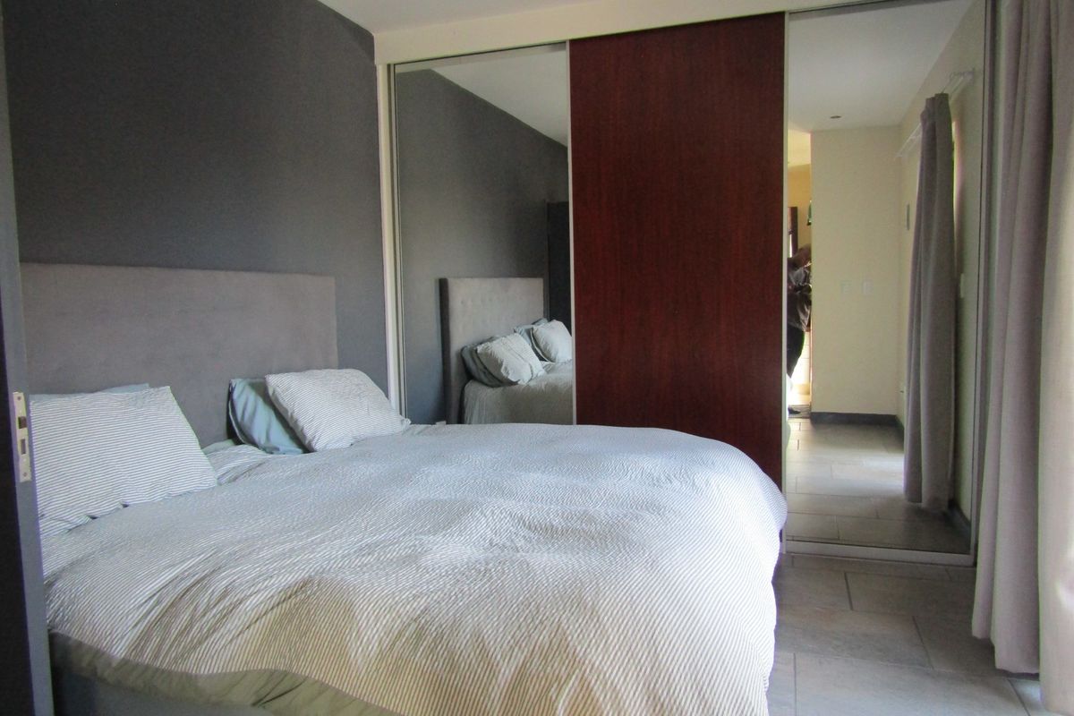 A bedroom featuring tiled flooring, a built-in mirrored wardrobe, and a dark accent wall, providing a functional and neutral living space.