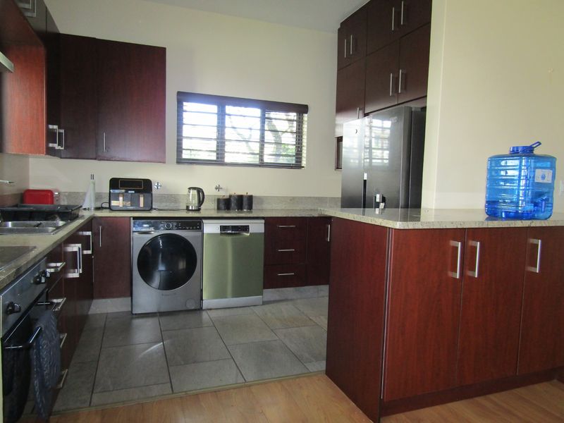A functional kitchen featuring dark wood cabinetry, granite countertops, tiled flooring, and integrated appliances, including a built-in oven and hob.