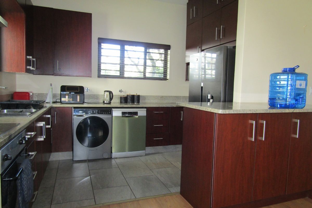 A functional kitchen featuring dark wood cabinetry, granite countertops, tiled flooring, and integrated appliances, including a built-in oven and hob.