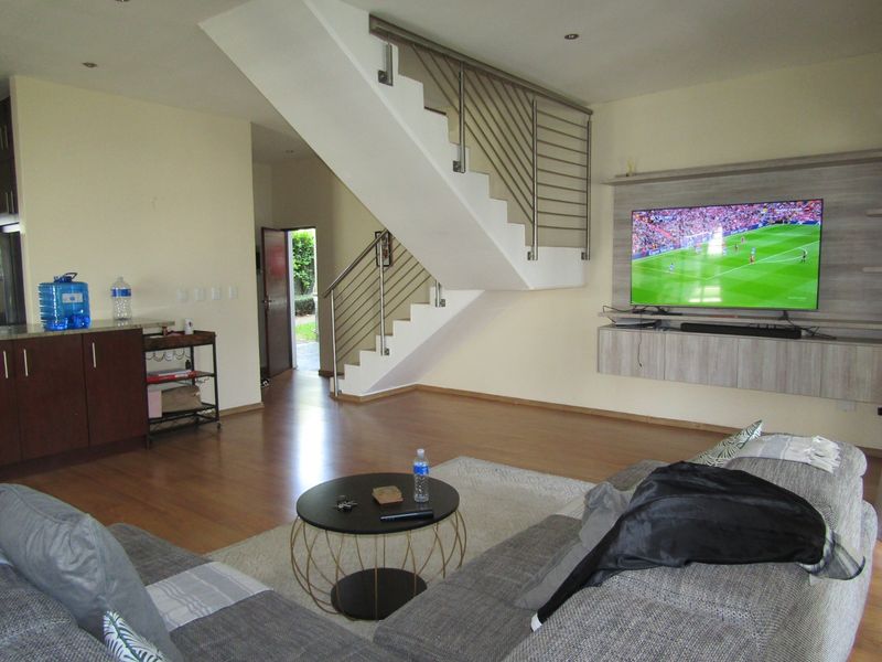 Open-plan living area featuring a modern staircase with stainless steel balustrades, laminate flooring, and a built-in media console.