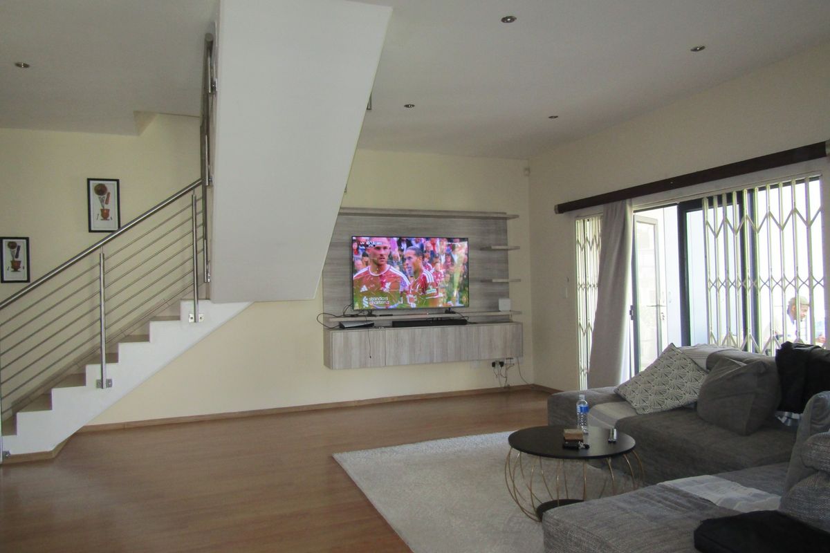 Spacious living room featuring laminate flooring, a modern staircase with stainless steel balustrades, and a built-in media console with access to a patio.