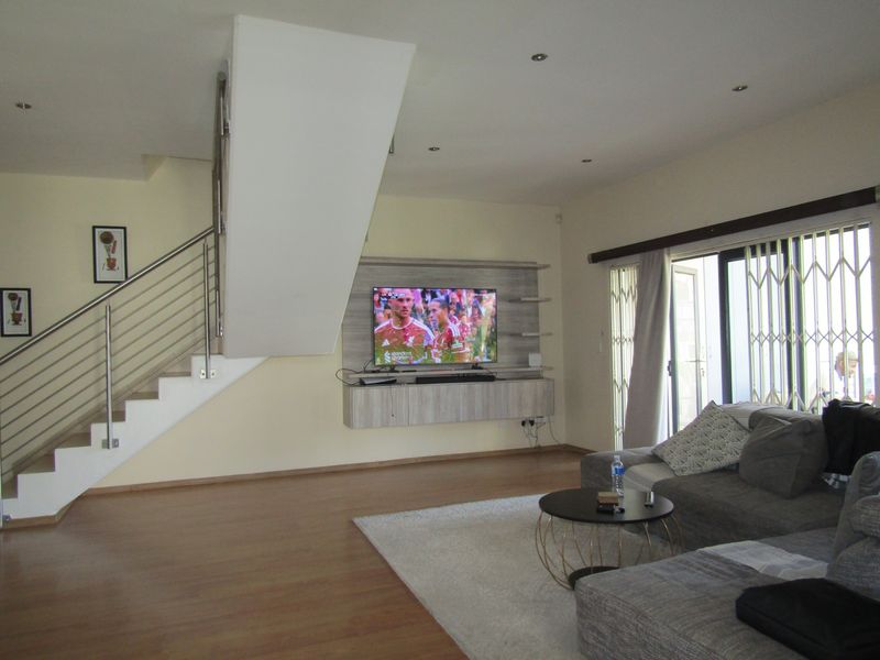 Spacious living room featuring laminate flooring, a modern staircase with stainless steel balustrades, and a built-in media console with access to a patio.