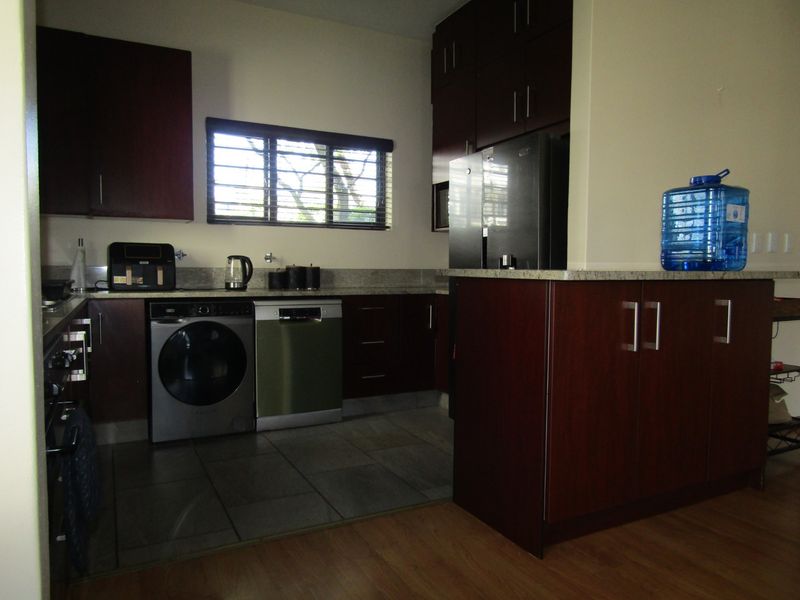 A functional kitchen featuring dark wood cabinetry, granite countertops, built-in oven, and integrated dishwasher, with tiled flooring and natural light from the window.