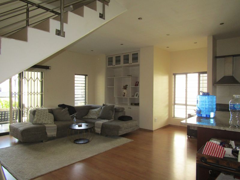 Spacious open-plan living area featuring laminate flooring, built-in shelving, and a modern staircase, seamlessly connecting to the kitchen space.