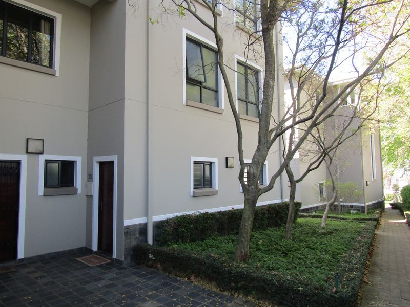 Front exterior view of the apartment building featuring a paved entrance, landscaped garden area, and modern casement windows.