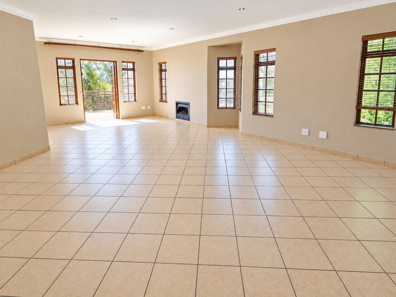 Spacious, light-filled living area featuring neutral tiled flooring, a built-in fireplace, and direct access to an outdoor balcony through double doors.
