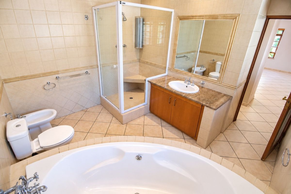 Spacious bathroom featuring a corner bathtub, separate glass-enclosed shower with built-in seat, vanity with granite countertop, toilet, and bidet.
