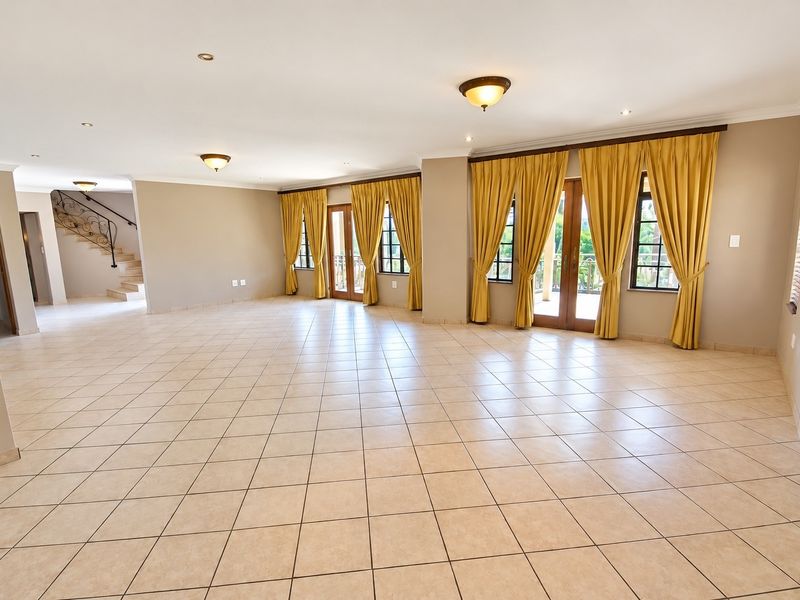 Spacious, open-plan living area featuring neutral tiled flooring, recessed lighting, and direct access to an outdoor patio through double french doors.