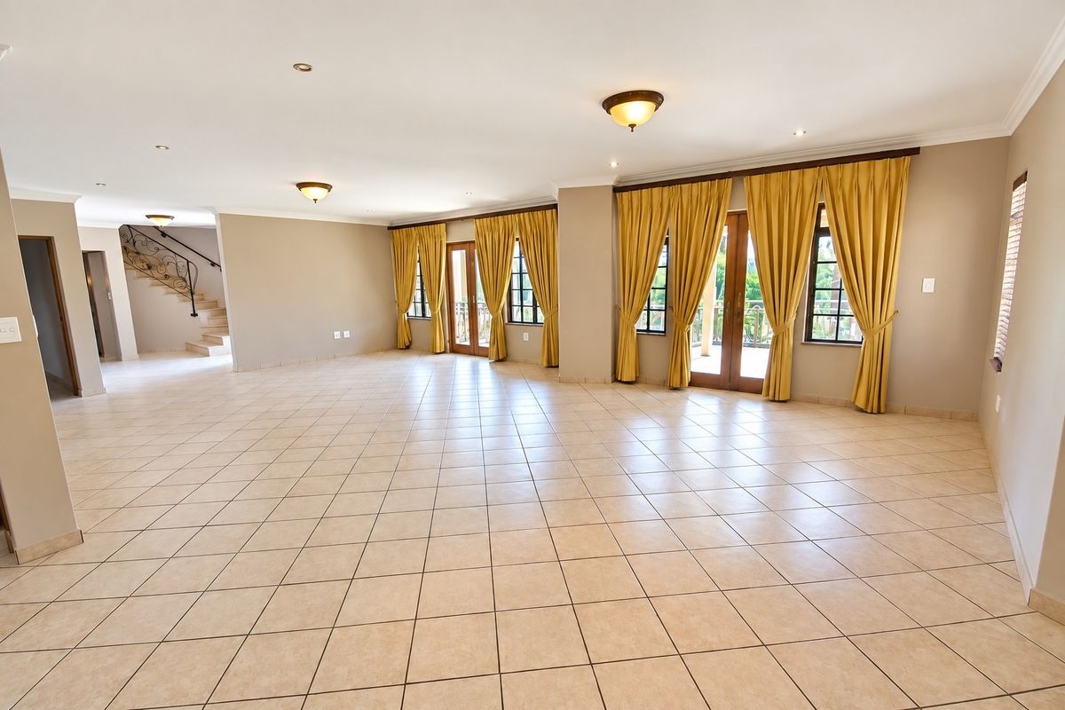 Spacious, open-plan living area featuring neutral tiled flooring, recessed lighting, and direct access to an outdoor patio through double french doors.
