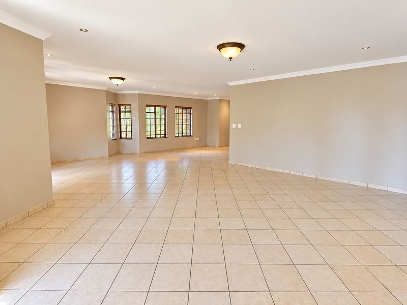 A spacious, vacant open-plan living area featuring neutral wall tones, tiled flooring, and ample natural light through timber-framed windows.