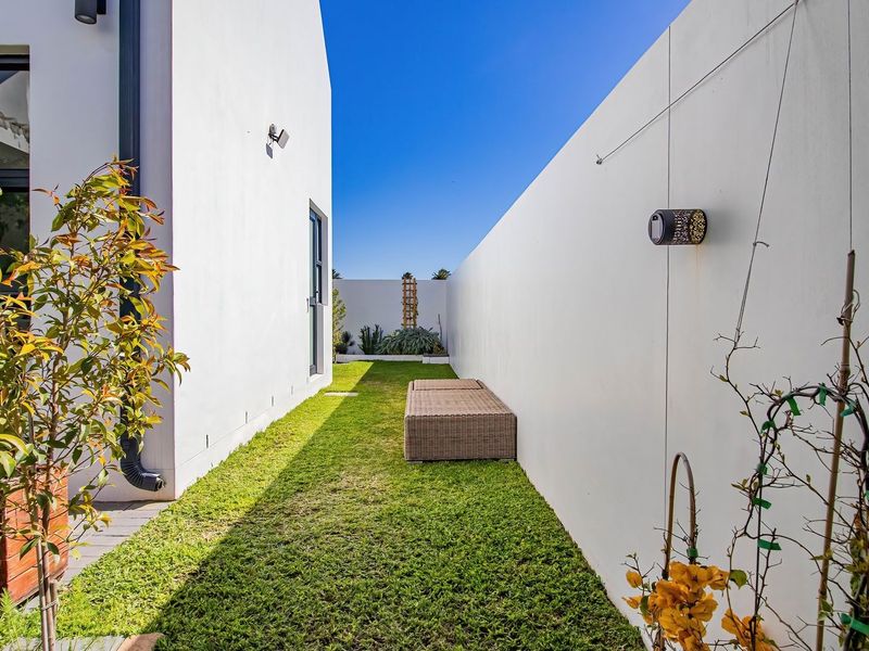 A well-maintained side garden passage featuring a manicured lawn, high boundary walls, and modern exterior lighting.