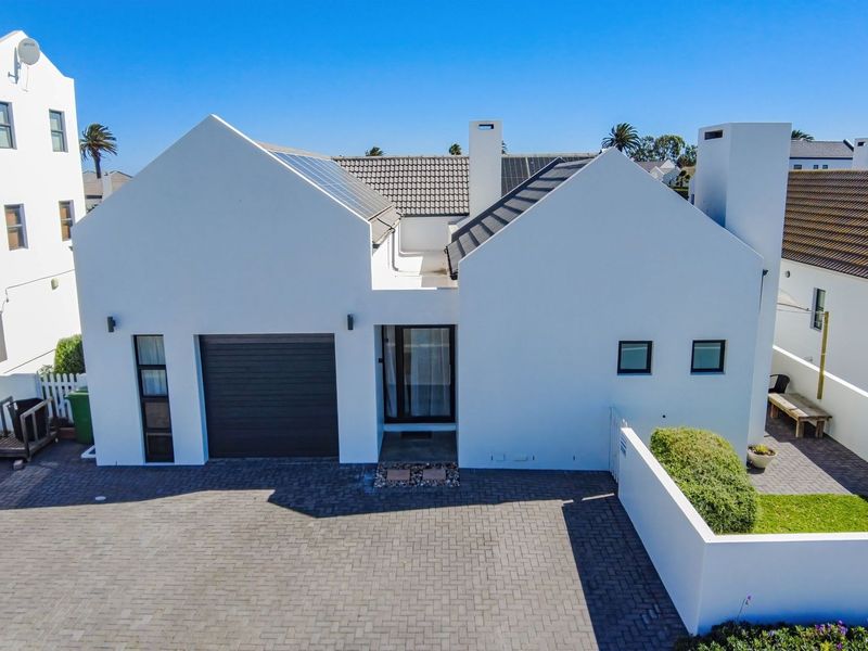 A modern, well-maintained house exterior featuring a paved driveway, integrated garage, and solar panels on a tiled roof.